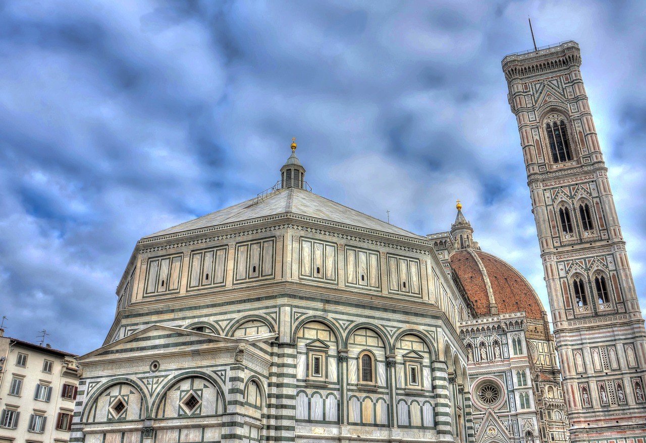 Tall white building with a tower and dome, to the right of it is another large building, both are under a cloudy sky